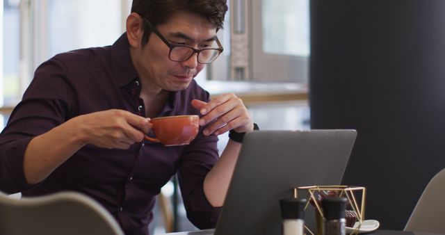 Asian businessman sipping coffee while working on laptop in modern office - Download Free Stock Images Pikwizard.com