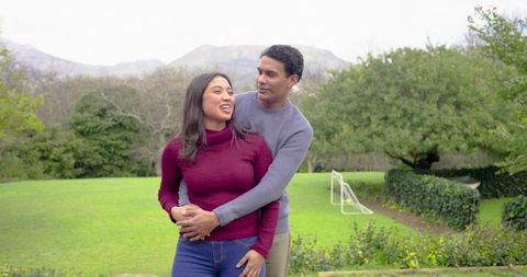 Diverse Couple Embracing on Park Lawn Laughing Together Near Small Soccer Goal Autumn