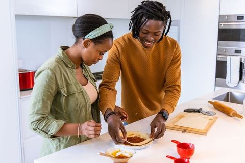 African american couple preparing pizza on modern white kitchen island, teamwork and joy