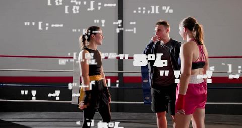 Trainer coaching two female boxers in ring holding blue pad during sparring session
