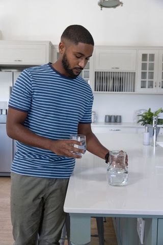 Man Pouring Water from Pitcher in Modern Kitchen