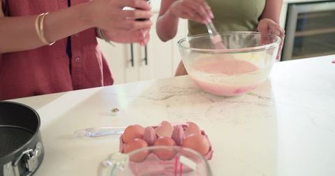 Friends whisking pastel batter on marble island baking together in cozy modern kitchen