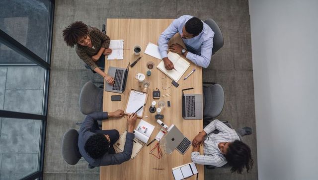 Overhead view of diverse team collaborating around modern conference table with laptops