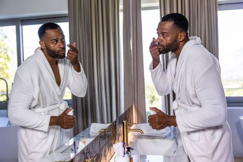 Mature african american man applying facial cream at marble vanity wearing white bathrobe