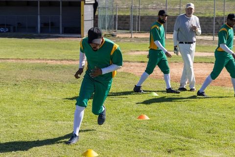 Baseball players sprinting through cone drill on sunny field while coach observes practice