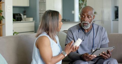 Home healthcare nurse consulting with patient about medication management on sofa