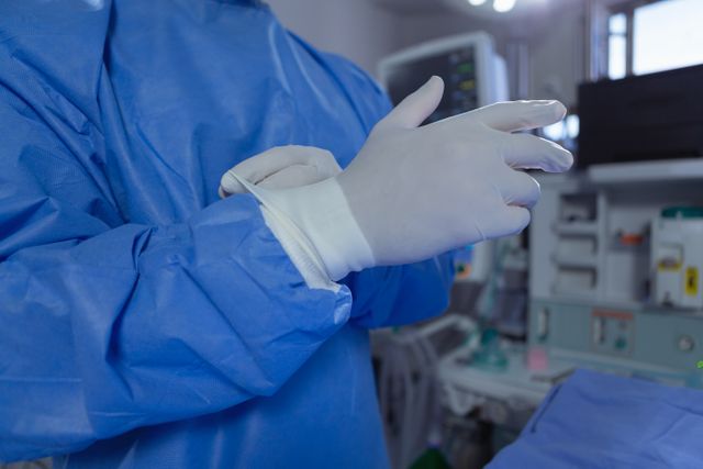 Mid section of male surgeon wearing surgical gloves while standing in operation room at hospital