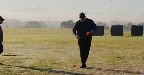 Dawn fitness drills placing orange disc cones on dewy sports field by two teammates
