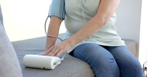Asian woman taking blood pressure with digital monitor at home