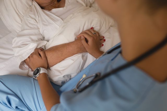 Female doctor in blue scrubs holding and consoling a senior woman in a bedroom. Ideal for use in healthcare, elderly care, home care services, and medical support contexts. Highlights compassion and professional care in a home setting.