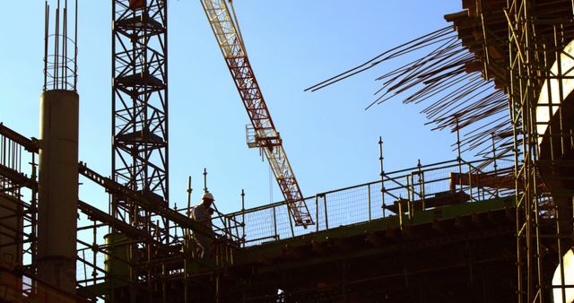 Construction workers, middle-aged, are busy at a construction site with a crane towering in the background, with copy space. Their hard hats and safety gear indicate strict adherence to safety protocols while working on the skeletal framework of a new building.