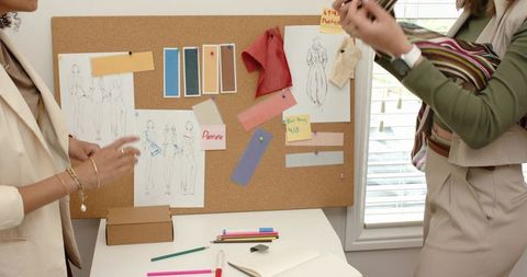 Female fashion designers collaborating over sketches and fabric swatches on cork board