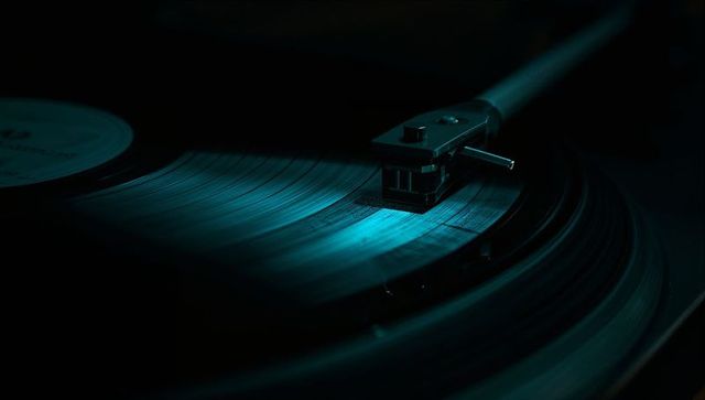 Moody teal turntable closeup showing spinning vinyl grooves and tonearm stylus detail