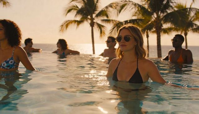 Woman soaking in infinity pool at tropical sunset resort with palm tree reflections