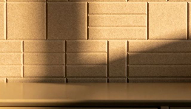 Warm sunlight casting geometric shadows on textured tan wall panels above kitchen countertop
