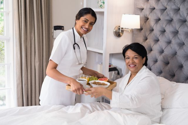 Portrait of smiling nurse serving breakfast to patient resting on bed at home
