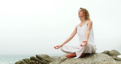 Caucasian Woman Meditating in Yoga Pose by Sea Outdoors
