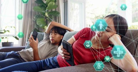 Asian Couple Reclining on Sofa Using Smartphones with Telehealth Hex Icons and Connectivity