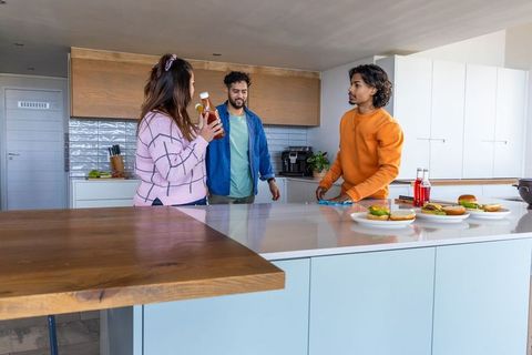 Diverse friends gathering at modern kitchen island preparing burgers and choosing condiments