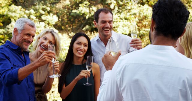 Friends enjoying a cheerful outdoor celebration while holding champagne glasses. Perfect for illustrating social gatherings, celebrations, diversity, happiness, and friendship. Suitable for use in lifestyle blogs, social event promotions, and marketing materials focused on celebrations and social interaction.