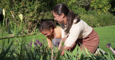 Woman and girl gardening together kneeling planting lavender in backyard with watering can
