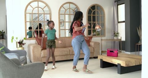Joyful mother and daughter dancing in modern living room with pink portable speaker