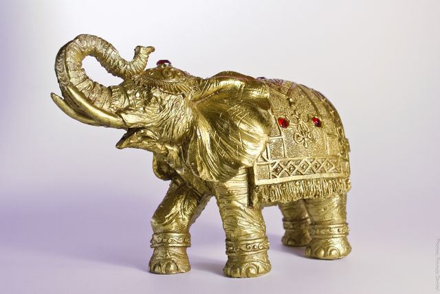 Golden decorative elephant statue with intricate ornamental details on both sides, adorned with red jewels. Ideal for home decor, symbolic representation of strength and power in various cultures, particularly Asian and Indian. Perfect for interior decoration, gifts, cultural events, or as a collectible piece.