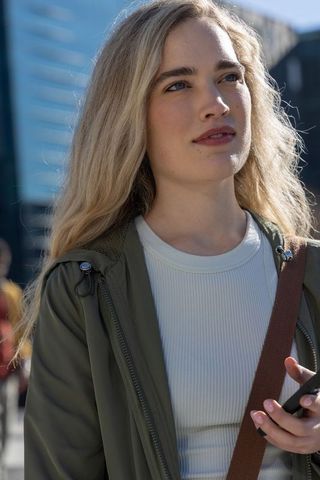 Young woman gazing upward on urban street holding smartphone in olive jacket