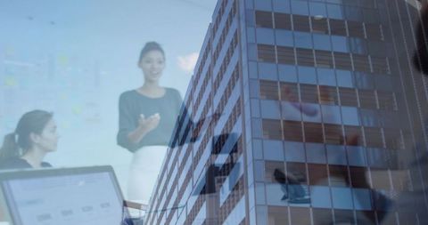 Presenting leader guiding team meeting with glass building reflection, laptop and smartphone