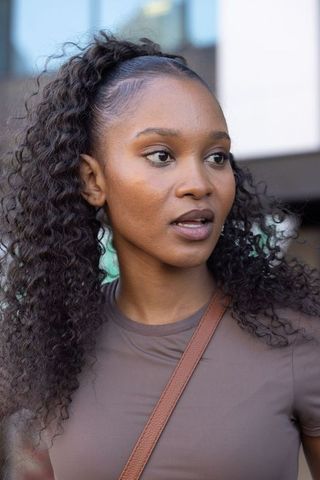 Young african woman speaking on urban street wearing fitted brown top and crossbody bag