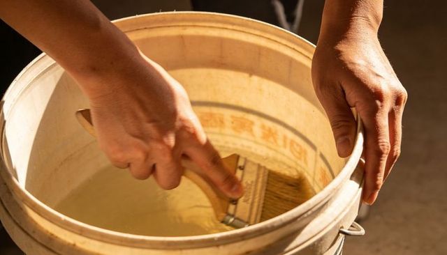 Dipping paint brush into bucket of water hands gripping rim preparing brush for painting