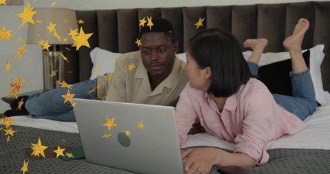 Couple streaming on laptop while lying on bed, relaxing at home with decorative gold stars