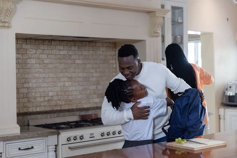 African american father hugging daughter in kitchen while packing backpack for school