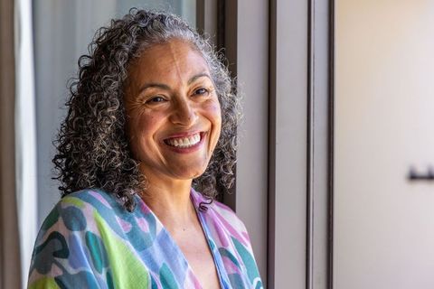 Mature african american woman smiling by window in pastel patterned robe, natural light