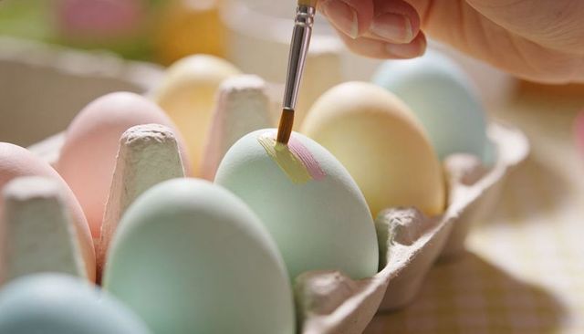 Hand painting pastel easter egg with brush in egg carton close-up craft moment