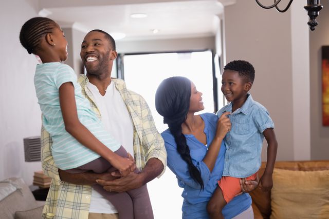 This image depicts a joyful African American family spending quality time together in their living room. The parents are carrying their children, all smiling and enjoying each other's company. Ideal for use in advertisements, family-oriented content, parenting blogs, and lifestyle articles.