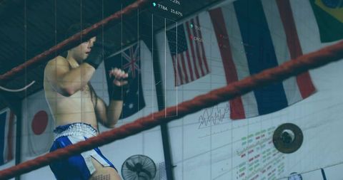 Standing boxer holding fists up in ring wearing blue trunks and black wraps, gym flags
