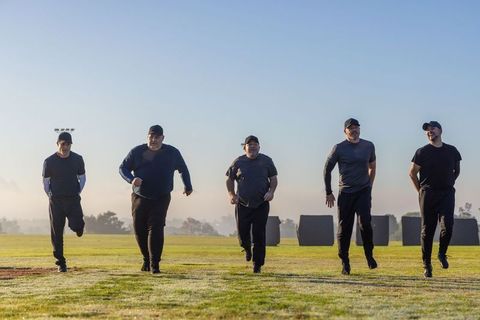 Men running together at dawn for team fitness training on grassy field
