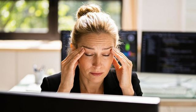 Midcareer woman experiencing headache while coding under work pressure at office desk