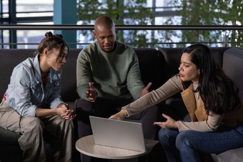 Multicultural team collaborating around laptop in modern office lounge discussing project