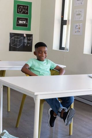 African american boy sitting smiling at classroom desk wearing light green tee and shoes