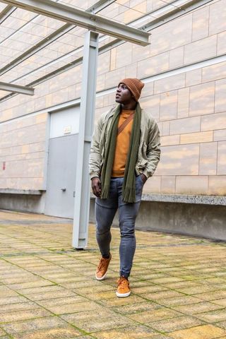 African american man walking in urban plaza wearing beanie scarf bomber jacket autumn