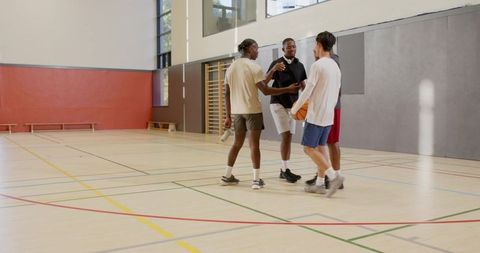 Diverse teammates greeting and planning next play in empty indoor basketball gym
