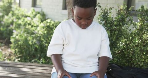 Contemplative african american boy sitting on bench in sunlit courtyard