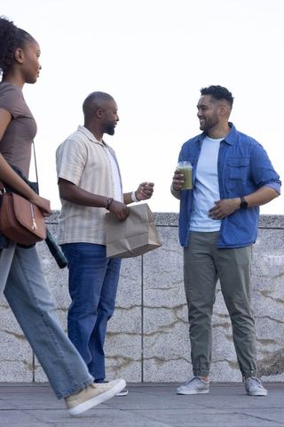 African american friends chatting on urban terrace holding smoothie and takeout bag