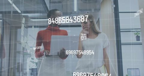 Female colleagues reviewing data on laptop with augmented reality overlay in glass office