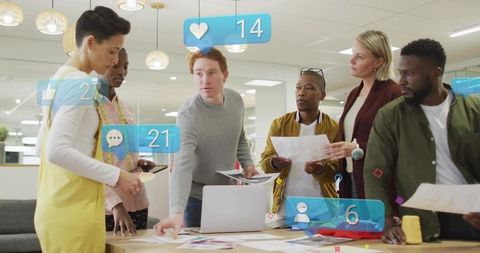 Diverse creative team collaborating around laptop with augmented reality social icons