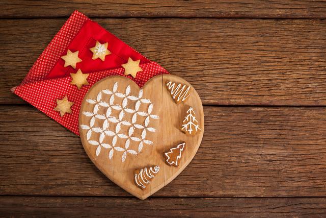 Christmas cookies and gingerbread on a wooden table with a heart-shaped board and red napkin. Ideal for holiday-themed advertisements, festive greeting cards, baking blogs, and seasonal social media posts.