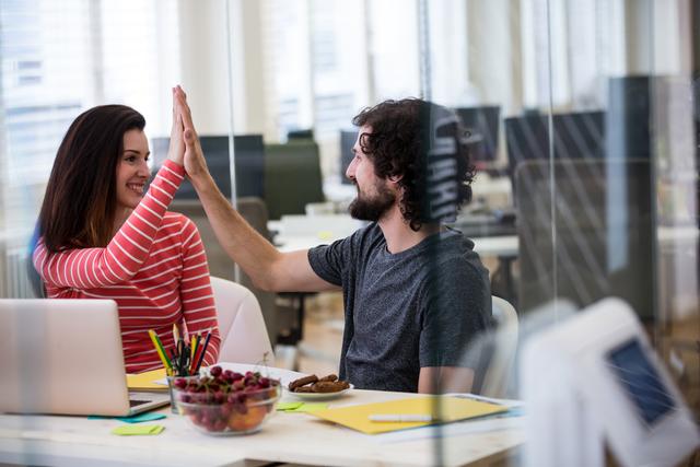 Male and female graphic designers giving high five to each other in office
