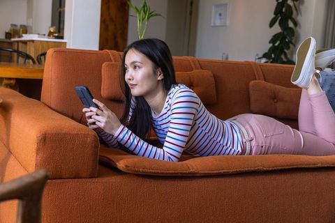 Relaxed woman lying on orange sofa looking at phone in modern living room